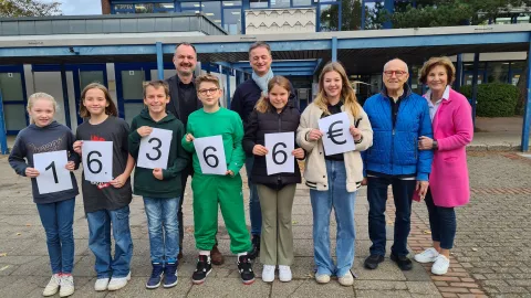 Schüler mit Zahlenkarten flankiert von Erwachsenen auf Schulhof 