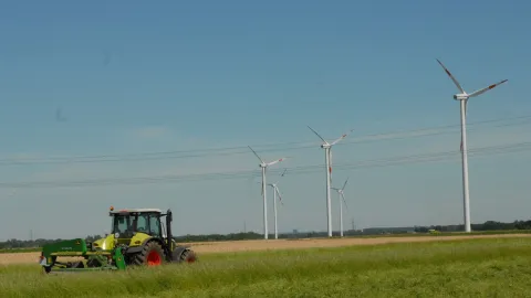 Schlepper auf Feld vor Windrädern 